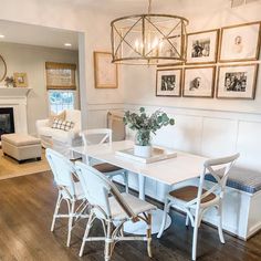 a dining room table with white chairs and pictures on the wall above it in a living room