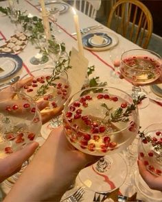 people holding wine glasses filled with food and garnished with greenery on the table