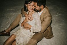 a man and woman sitting on the ground hugging each other with their arms around each other