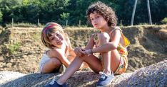 two young children sitting on top of a rock