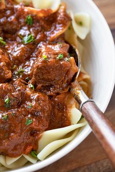 a white bowl filled with pasta and meat covered in sauce, garnished with parsley