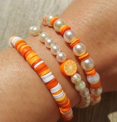 three bracelets with orange, white and pearl beads on the wrist are shown in close up