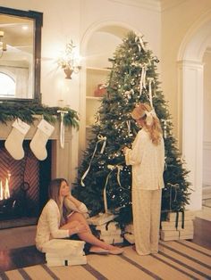 two women sitting in front of a christmas tree