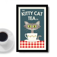 a cup of coffee next to a framed poster with a cat in the teacup