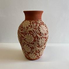 a brown and white vase sitting on top of a table next to a wall in the background