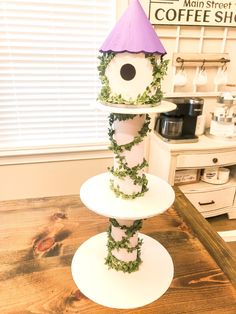 three tiered birdhouse decorated with greenery and purple hat on wooden table in kitchen