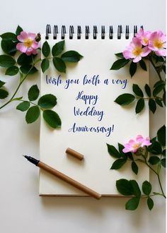 a notepad with writing on it next to some flowers and a pen, which reads wish you both a very happy wedding anniversary