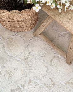 a wooden bench sitting next to a basket filled with flowers on top of a tiled floor