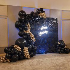 black and gold balloons are arranged in the shape of an arch with words on it