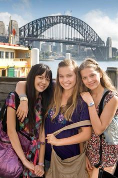 three girls standing next to each other in front of the sydney harbour bridge and opera house