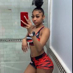 a woman taking a selfie in the bathroom with her cell phone while wearing red and black bathing suit