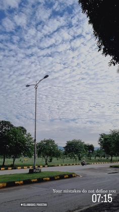 an advertisement for a street light on the side of a road with clouds in the sky