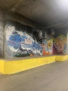 graffiti is painted on the side of a building under an overpass in a parking lot