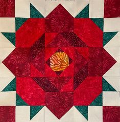 a red and white quilted piece with green leaves in the center on a table