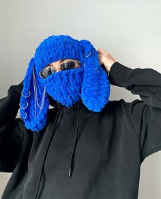 a person wearing a blue knitted animal mask covering their face with his hands and sunglasses