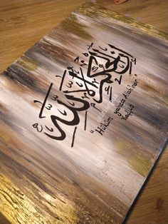 a painting with arabic writing on it sitting on top of a wooden table next to scissors