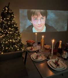 a table with plates and glasses on it in front of a christmas tree that is lit up