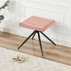 a pink stool sitting on top of a wooden floor next to a potted plant