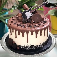 a chocolate cake with white frosting and guitar decoration on top, surrounded by potted plants