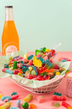 a bowl filled with lots of colorful candy next to a bottle of orange juice on a table