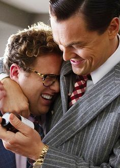 two men in suits are hugging each other and smiling at something on the camera screen