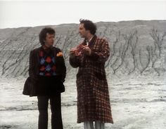 two men standing next to each other in front of a rock formation and eating food