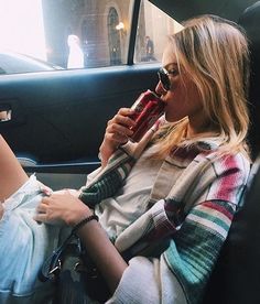 a woman sitting in the back seat of a car talking on a cell phone while holding a cup