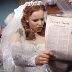 a woman in a wedding dress reading a newspaper while wearing a tiara and veil