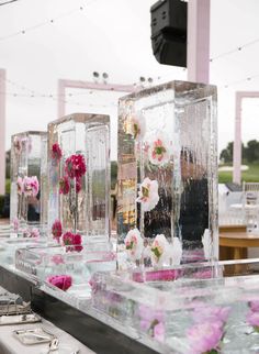 several clear vases filled with pink flowers on top of a metal table covered in ice