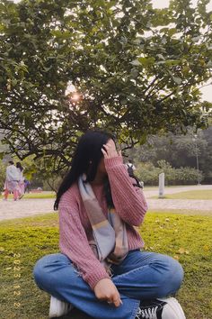 a woman sitting on the ground talking on her cell phone in front of a tree