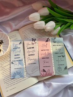 three bookmarks with words on them next to tulips and an open book