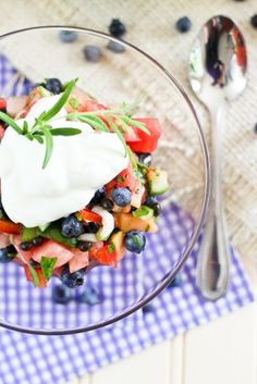 a glass bowl filled with blueberries, cucumber and sour cream on top of a checkered cloth