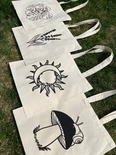 four tote bags with designs on them laying in the grass, all lined up