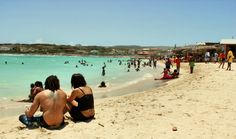 several people are sitting on the beach and swimming in the blue water at this time