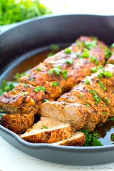 meat and vegetables in a skillet on a white table with green garnish