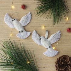 two white doves are sitting on a table next to pine cones and christmas lights