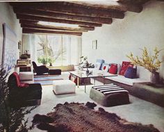 a living room filled with furniture next to a window covered in plants and rugs