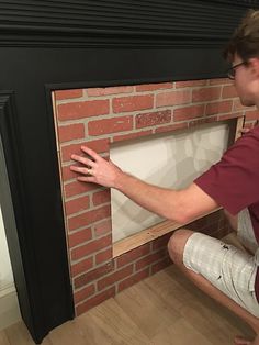 a man sitting on the floor in front of a brick fireplace with his hands out