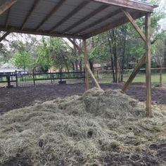 a pile of hay sitting under a wooden structure in the middle of a park area