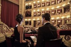 a man and woman sitting in front of a stage with red curtains on the walls