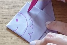 someone is making an origami fish out of paper on a wooden table with a pink pen