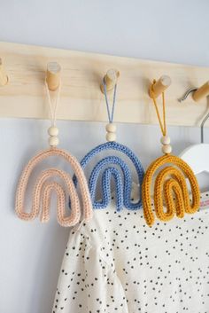 three crocheted rainbows hang on a coat rack with clothes pins and pegs