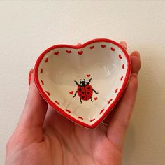 a hand holding a heart shaped bowl with a ladybug painted on the side