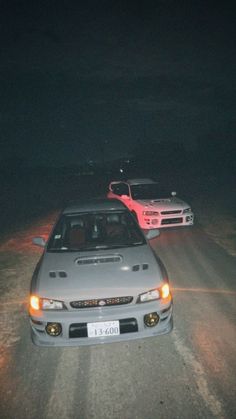 two cars parked on the side of a road in the dark with their lights on