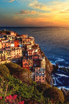 the sun is setting over an ocean and some buildings on top of a cliff by the water