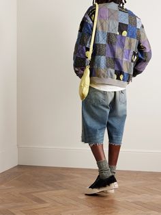 a man with dreadlocks standing in front of a wall wearing a colorful jacket