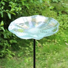 a glass dish sitting on top of a metal stand in the grass next to trees