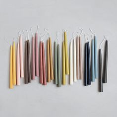 several different colored candles are lined up on a white surface with string attached to them