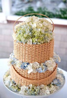 a three tiered cake decorated with flowers and wicker basket on the top layer