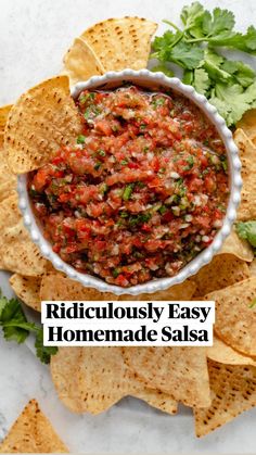 a white bowl filled with salsa surrounded by tortilla chips and cilantro